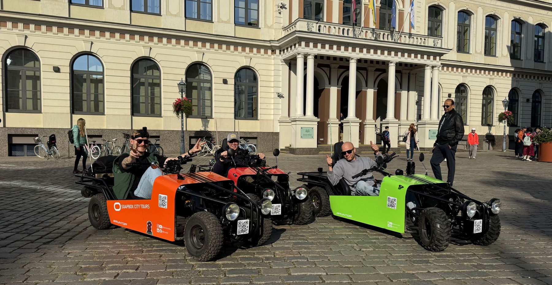 Three smiling riders outside Riga City Hall